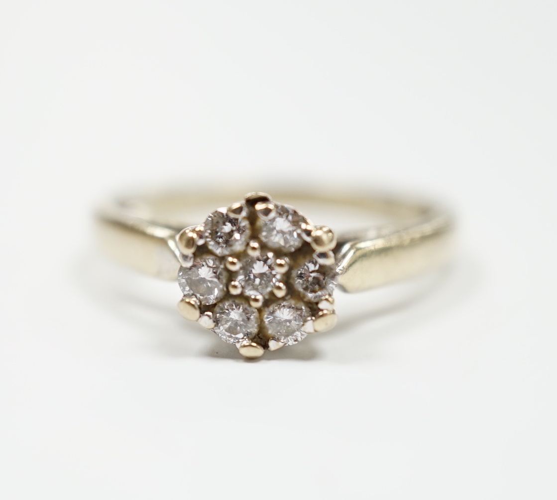 A 750 white metal and seven stone diamond set circular cluster ring, size M, gross weight 3.2 grams.